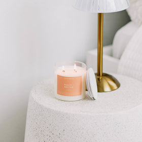 Candle with a peach label on a textured surface next to a gold lamp.
