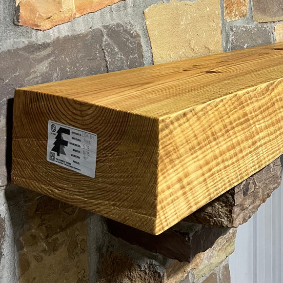 A beam style fireplace mantel, made from pine wood, mounted on a stone wall.