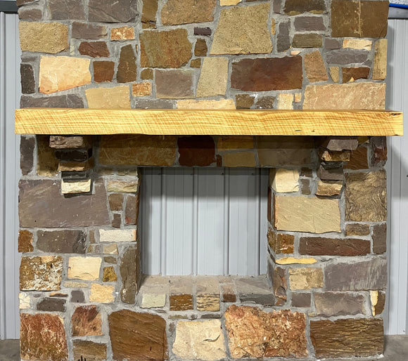 A beam style fireplace mantel, made from pine wood, mounted on a stone wall.