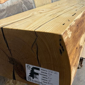 A live edge style fireplace mantel, made from ash wood, mounted on a stone wall.