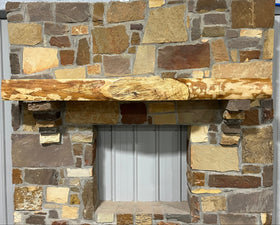 A live edge style fireplace mantel, made from ash wood, mounted on a stone wall.