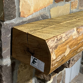 A live edge style fireplace mantel, made from ash wood, mounted on a stone wall.