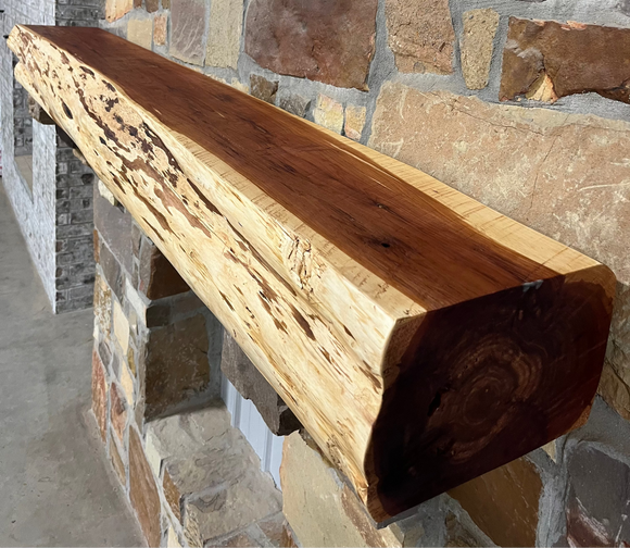 A live edge style fireplace mantel, made from cedar wood, mounted on a stone wall.
