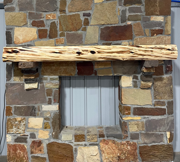A live edge style fireplace mantel, made from cedar wood, mounted on a stone wall.