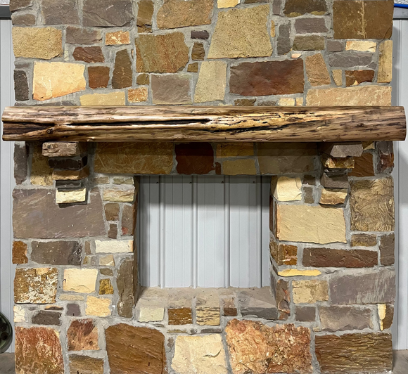 A live edge style fireplace mantel, made from walnut wood, mounted to a rock wall.