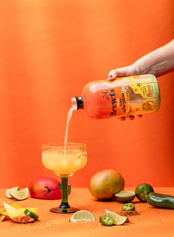 Bacardi Limon being poured into a glass with mangoes and limes on an orange background