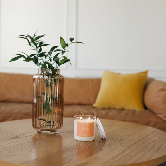 Candle and vase on a wooden table with a couch and yellow pillow in the background