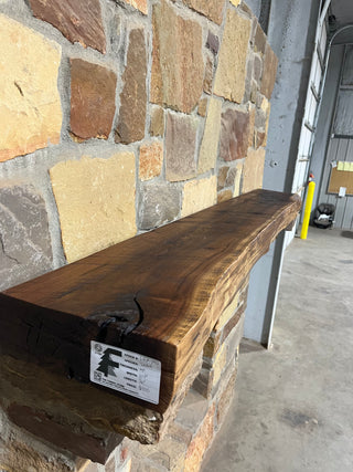 Live Edge Walnut Fireplace Mantel displayed on a stone wall, showcasing its smooth, dark-toned surface, ideal for contrasting with white stone fireplaces.