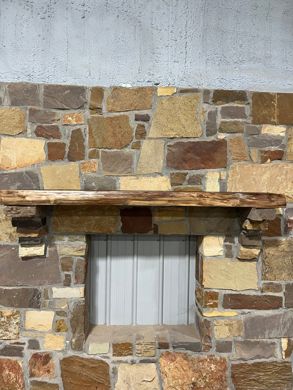 Live Edge Walnut Fireplace Mantel displayed on a stone fireplace with a wood shelf, showcasing its smooth, dark finish that complements the stone backdrop.