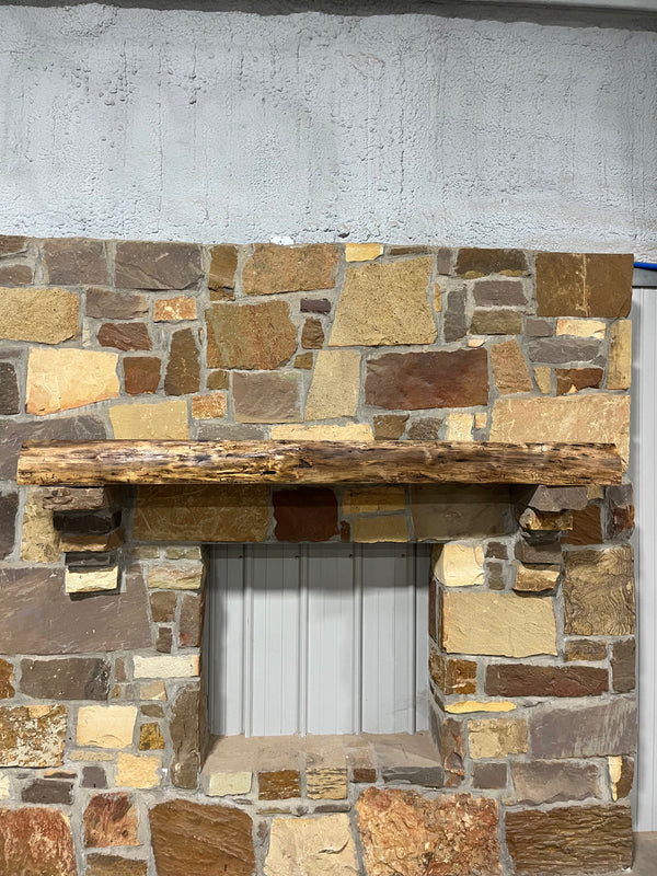 Live Edge Walnut Fireplace Mantel displayed on a stone wall, featuring a natural wood shelf above a white stone or shiplap fireplace, highlighting its dark tone and elegant finish.