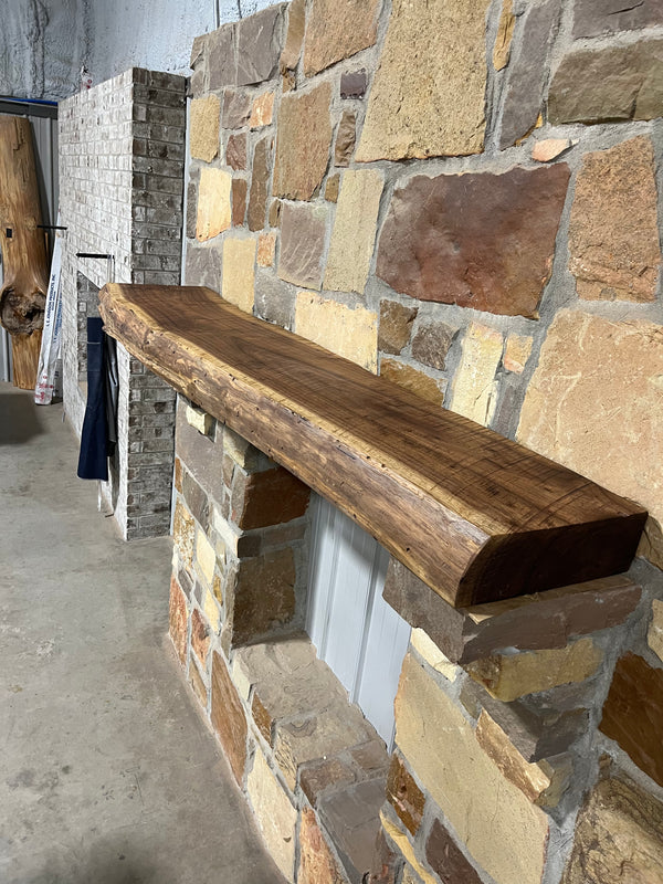 Live Edge Walnut Fireplace Mantel on a stone wall, showcasing its smooth finish and natural wood grain, complementing the stone's texture.