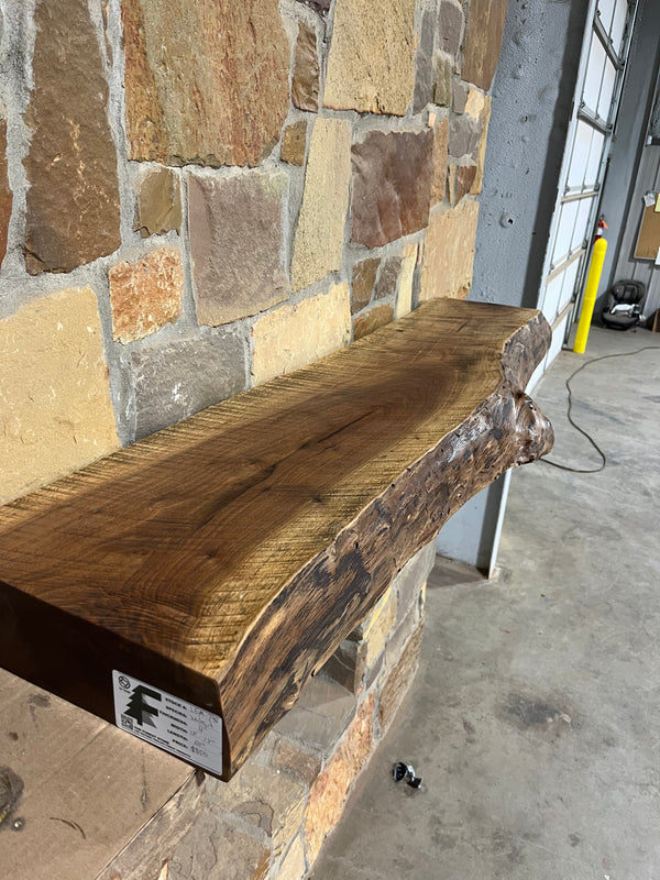 Beautiful, live edge, circle sawn surface of a walnut fireplace mantel sitting on stone corbels of a fireplace