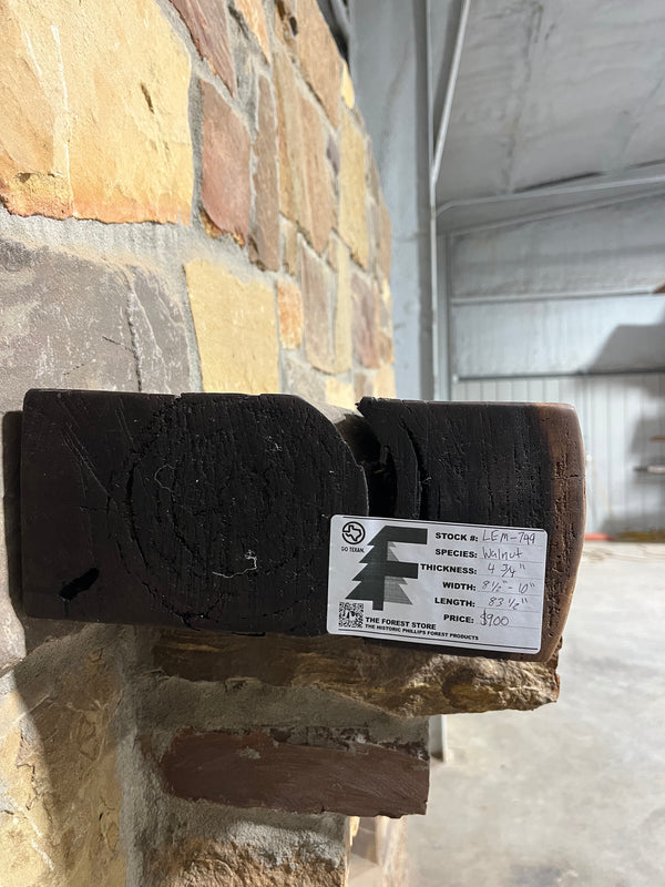 Dark, rustic end of a walnut mantel sitting on a stone corbel of a fireplace