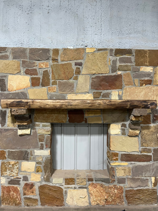 Front view of a rustic, live edged walnut sitting on a stone corbel of a beautiful fireplace