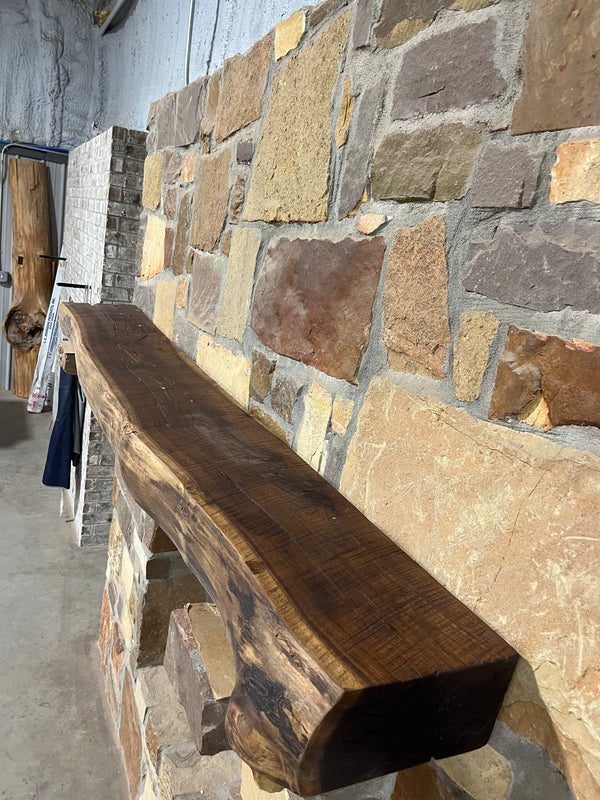 Right side of a beautiful, rustic live edge, circle sawn mantel sitting on stone corbels of a fireplace