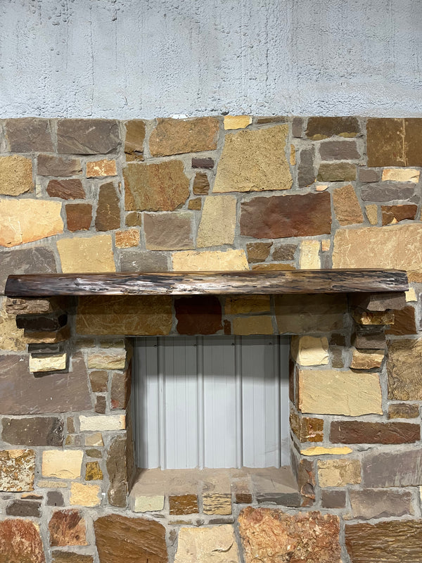 Live edge view of walnut mantel sitting on stone corbels of a fireplace