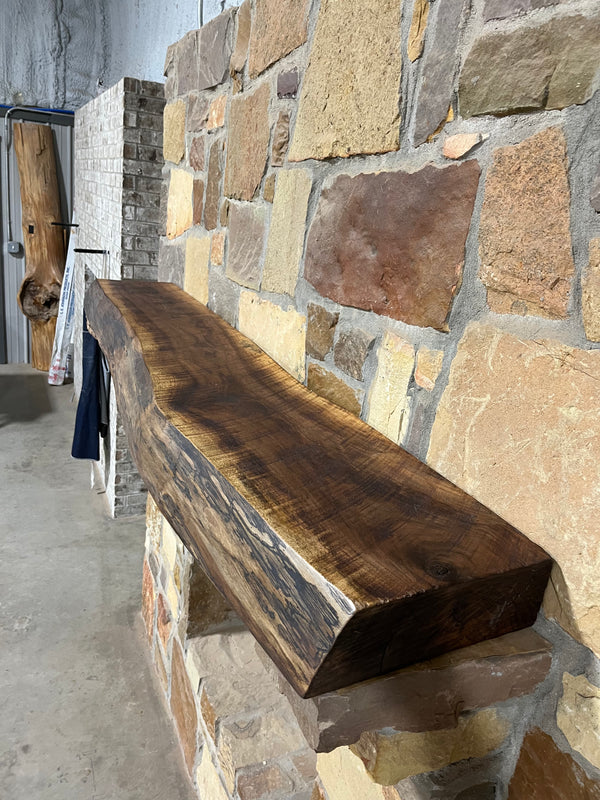 Circle sawn, walnut mantel containing beautiful live edge sitting on stone corbels of a fireplace