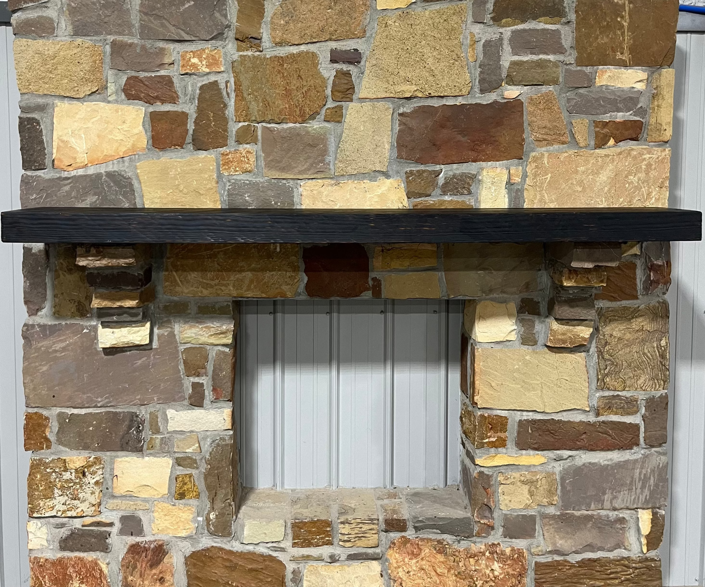 A burnt solid pine wood beam mantel mounted on a stone fireplace