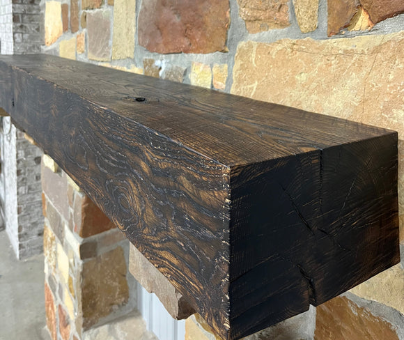 A burnt solid oak wood beam mantel mounted on a stone fireplace