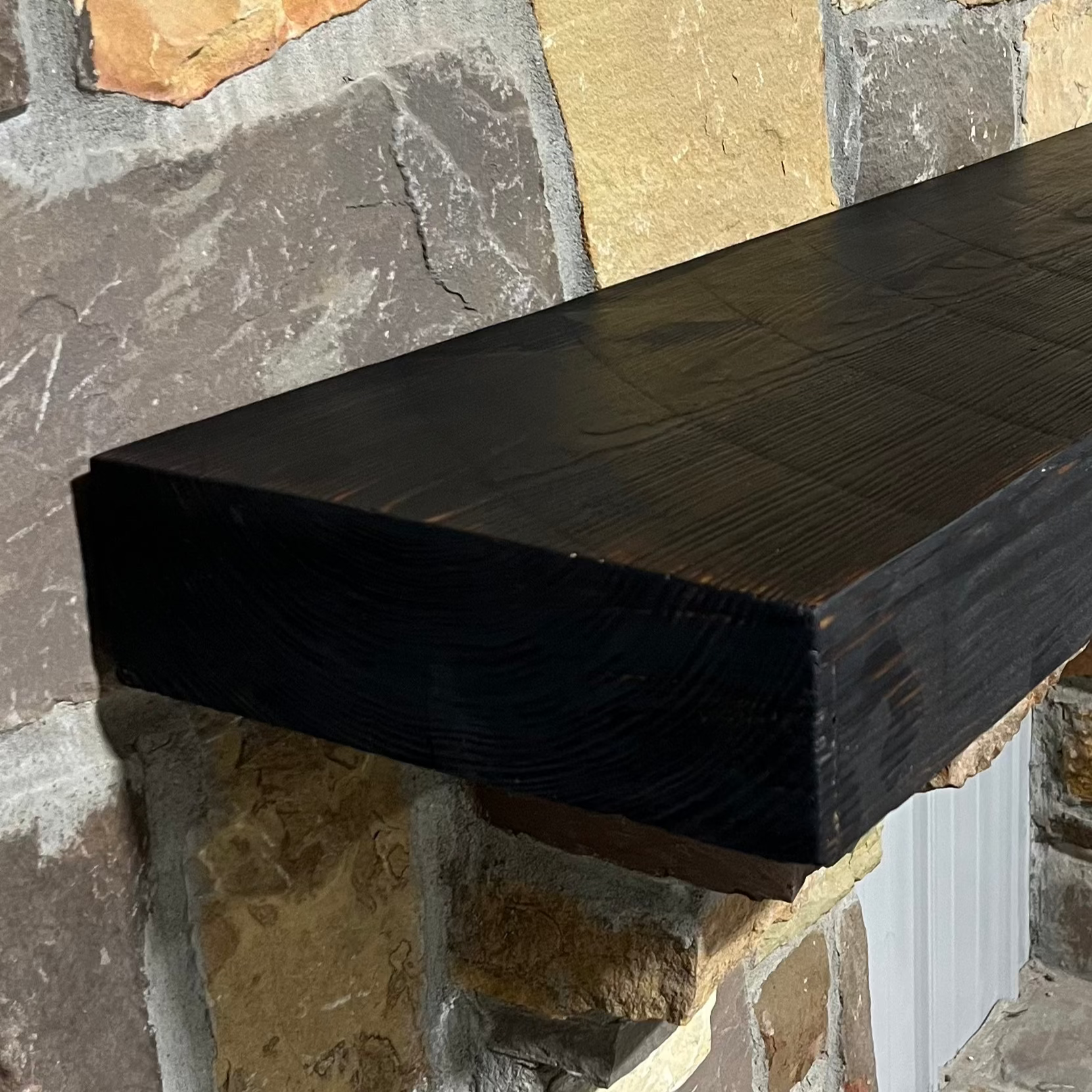 A burnt solid pine wood beam mantel mounted on a stone fireplace