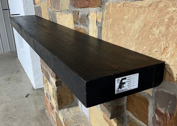 A beam style fireplace mantel, made from burned pine wood, mounted on a stone wall.