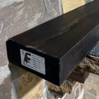 A beam style fireplace mantel, made from burned oak wood, mounted on a stone wall.