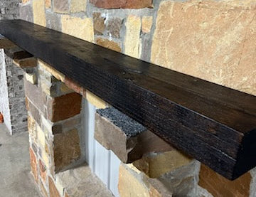 A beam style fireplace mantel, made from burned oak wood, mounted on a stone wall.