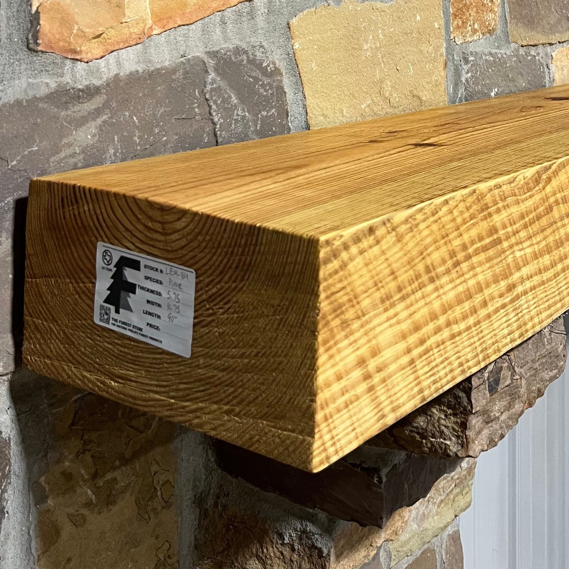 Solid pine beam fireplace mantel mounted on a stone wall.