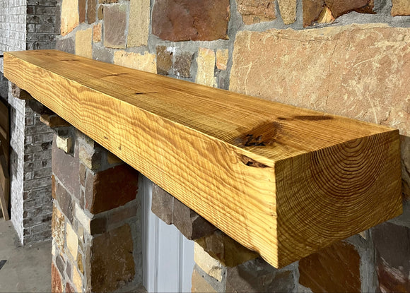 A beam style fireplace mantel, made from pine wood, mounted on a stone wall.