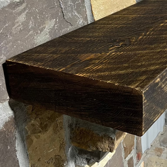 A beam style fireplace mantel, made from pine wood, mounted on a stone wall.