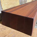 A beam style fireplace mantel, made from sapele wood, mounted on a stone wall.