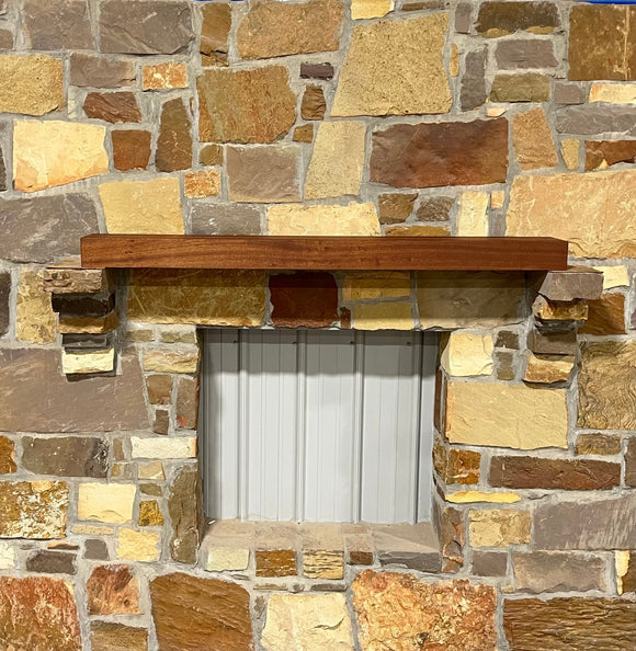 A beam style fireplace mantel, made from sapele wood, mounted on a stone wall.