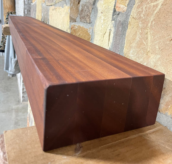 A beam style fireplace mantel, made from sapele wood, mounted on a stone wall.