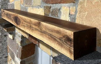 A beam style fireplace mantel, made from walnut wood, displayed on a rack.