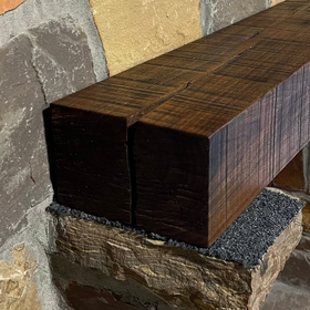 A beam style fireplace mantel, made from walnut wood, displayed on a rack.