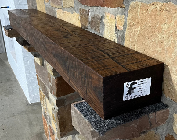 A beam style fireplace mantel, made from walnut wood, displayed on a rack.