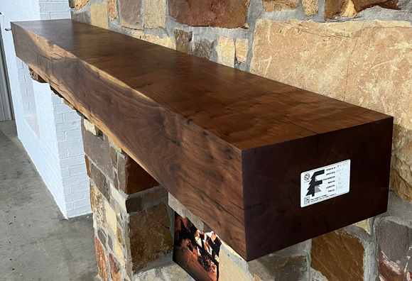A beam style fireplace mantel, made from walnut wood, displayed on a rack.