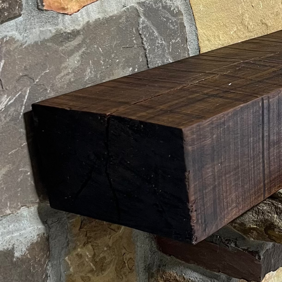 A beam style fireplace mantel, made from walnut wood, displayed on a rack.