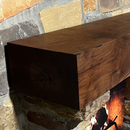 A beam style fireplace mantel, made from walnut wood, displayed on a rock wall.