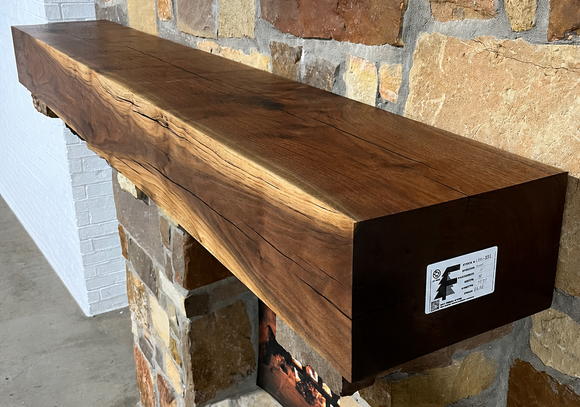 A beam style fireplace mantel, made from walnut wood, displayed on a rock wall.