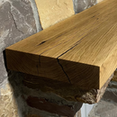 A beam style fireplace mantel, made from white oak wood, mounted on a stone wall.