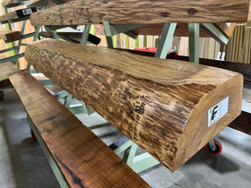 A live edge style fireplace mantel, made from ash wood, displayed on a rack.