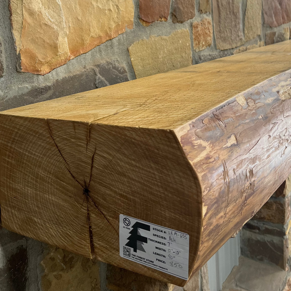 A live edge style fireplace mantel, made from ash wood, mounted on a stone wall.