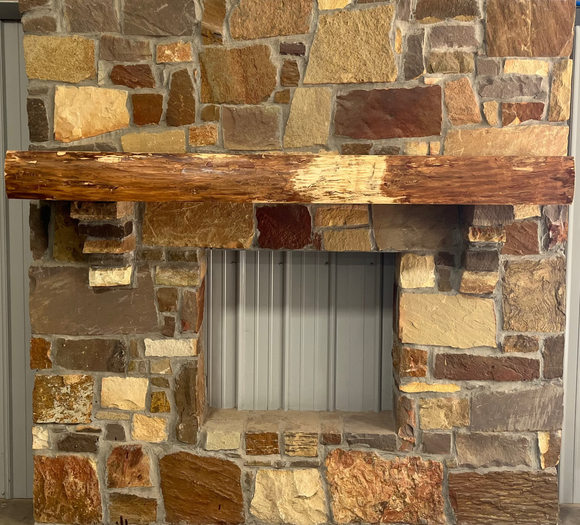A live edge style fireplace mantel, made from ash wood, mounted on a stone wall.
