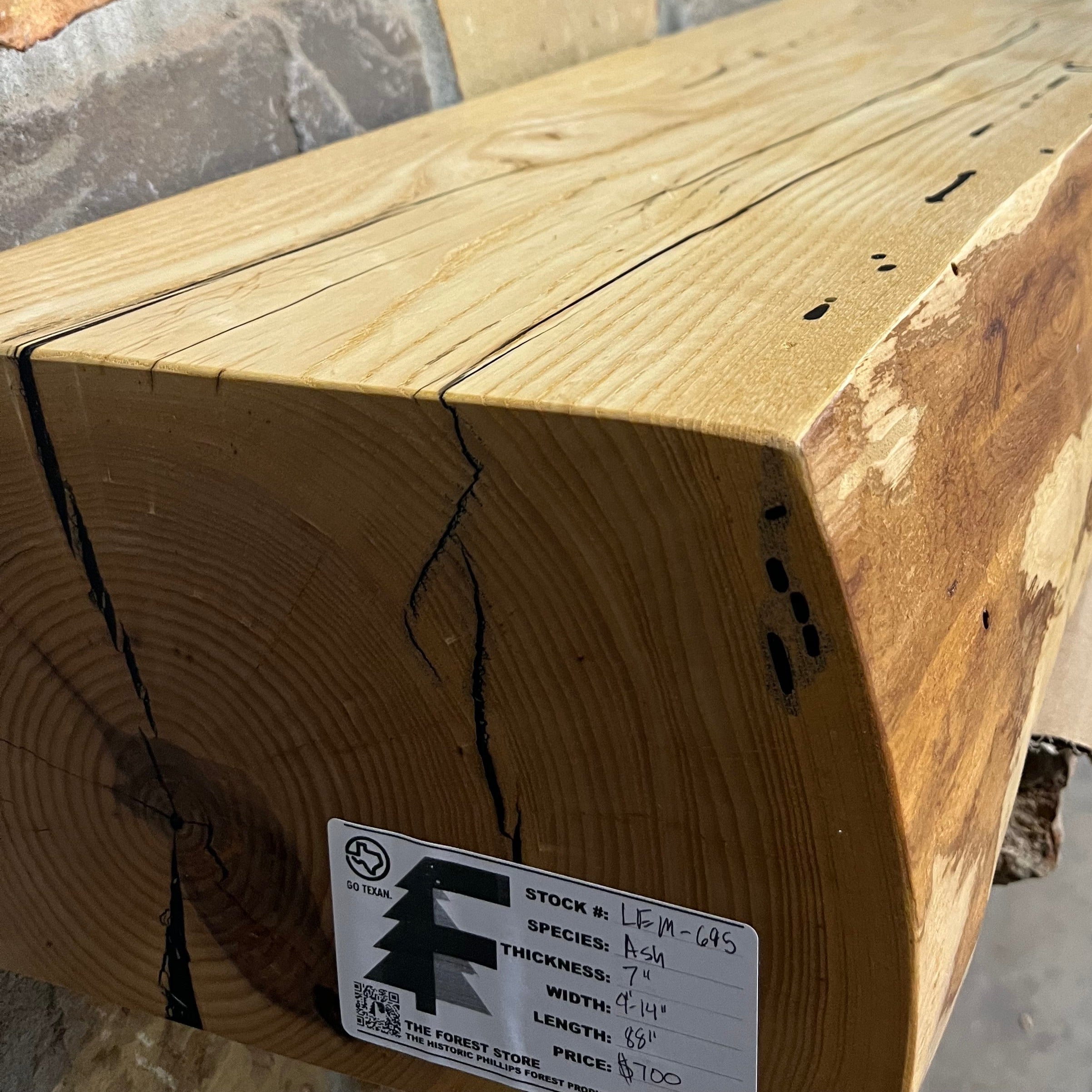 A live edge style fireplace mantel, made from ash wood, mounted on a stone wall.