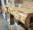A live edge style fireplace mantel, made from ash wood, mounted on a stone wall.
