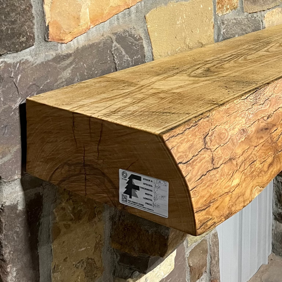 Solid live edge ash fireplace mantel mounted on a stone wall.
