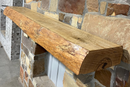 Solid live edge ash fireplace mantel mounted on a stone wall.