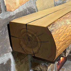 A live edge style fireplace mantel, made from ash wood, mounted on a stone wall.