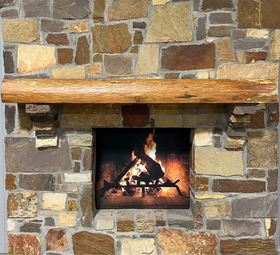 A live edge style fireplace mantel, made from ash wood, mounted on a stone wall.